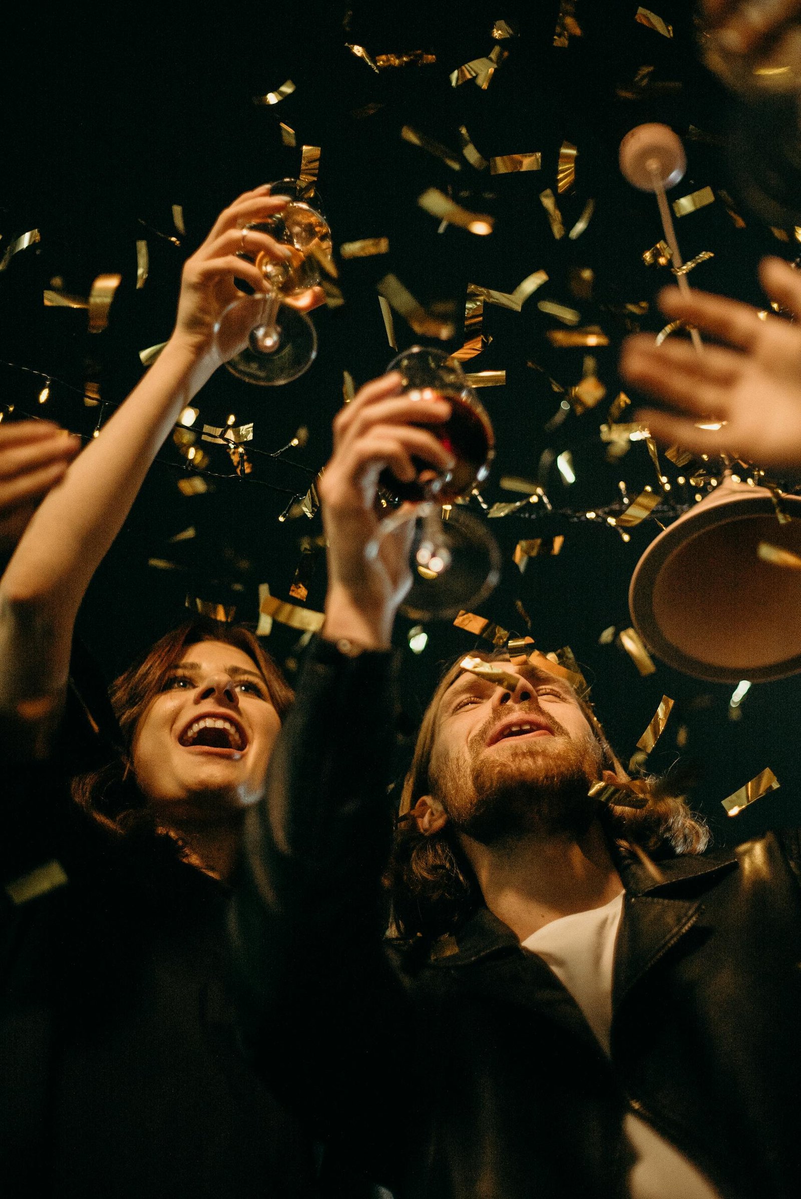 Group of friends enjoying New Year's Eve party with confetti and drinks.